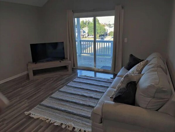 Relax in this cozy living space with a large flat-screen TV, comfortable sofa, and a beautiful view from the sliding glass door leading to the outdoor deck.
