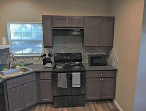 Kitchen features a central stove, microwave, and sink, with dark grey cabinets and a tiled backsplash.