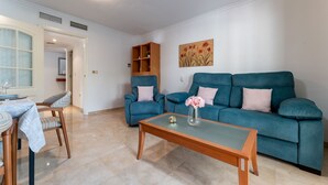 A living room with a blue sofa, a glass coffee table, and a dining area with a table and chairs. - MalagaSuite Costa Sol Oasis 2 (Torremolinos)