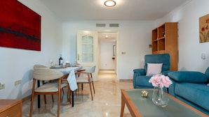 A living room with a dining area, a blue sofa, a vase with flowers, and a red abstract painting on the wall. - MalagaSuite Costa Sol Oasis 2 (Torremolinos)
