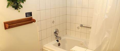 Un baño en esquina con bañera, un perchero de madera y un cartel en la pared.