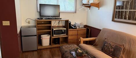 A compact living space with a sofa, a television, a microwave, and a small refrigerator.