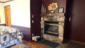 A cozy room with a stone fireplace, a quilted bedspread, and a decorative pine tree.