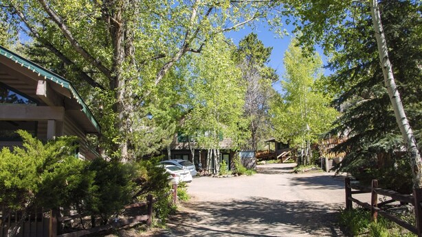 A lodge with a covered parking area, surrounded by trees and a wooden fence.