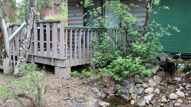 Eine Holzterrasse mit Geländer, ein kleiner Bach und ein Gebäude mit grüner Tür.