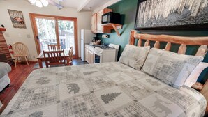 Ein Schlafzimmer mit einem großen Bett, einem Holzkopfstück, einem Schreibtisch mit Computer und Blick auf Birkenbäume durch das Fenster.