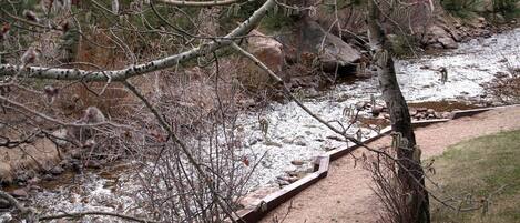 A river with a wooden walkway alongside it, surrounded by trees and rocks.