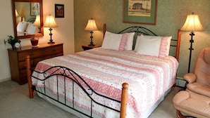 A bedroom with a bed, two bedside tables, a dresser, a chair, and a mirror. - Fawn Valley Inn: 240 2 Bedroom Condo (Estes Park)