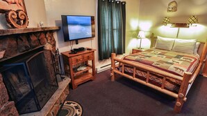 Une pièce confortable avec une cheminée, un lit recouvert d’une courtepointe, une télévision et une petite table de chevet en bois.