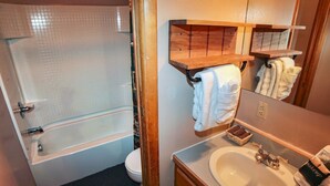 Une salle de bain avec une baignoire, des toilettes, un lavabo et une étagère en bois où sont posées des serviettes.