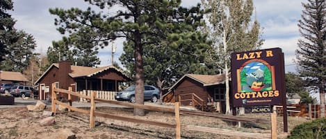 Opastekyltti, jossa lukee ”Lazy R Cottages”, ja jossa on kuvattuna maalaishenkinen puinen mökki, puinen aita ja kirkas taivas.