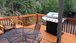 Una terraza de madera con una parrilla, una mesa redonda y sillas.