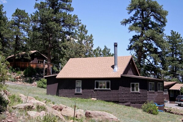 A rustic cabin with a chimney, surrounded by trees and rocks. - Lazy R Cottages: 6 2 Bedroom Cabin (Estes Park)