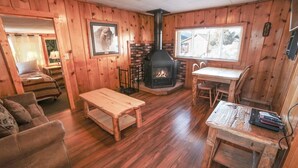 Un accogliente interno di una baita con camino, pareti in legno, un tavolo da pranzo e un divano.