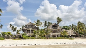 A beachfront property with two main buildings, each featuring a thatched roof and surrounded by palm trees. - Villa Malaika (Jambiani)