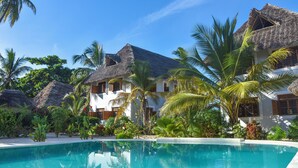 A resort with a swimming pool, thatched-roof buildings, and tropical vegetation. - Villa Malaika (Jambiani)