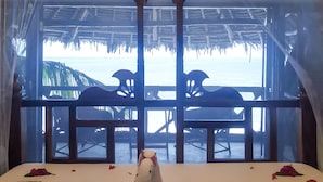 A room with a bed, a decorative hanging light, and a view of the beach through a window. - Villa Malaika (Jambiani)