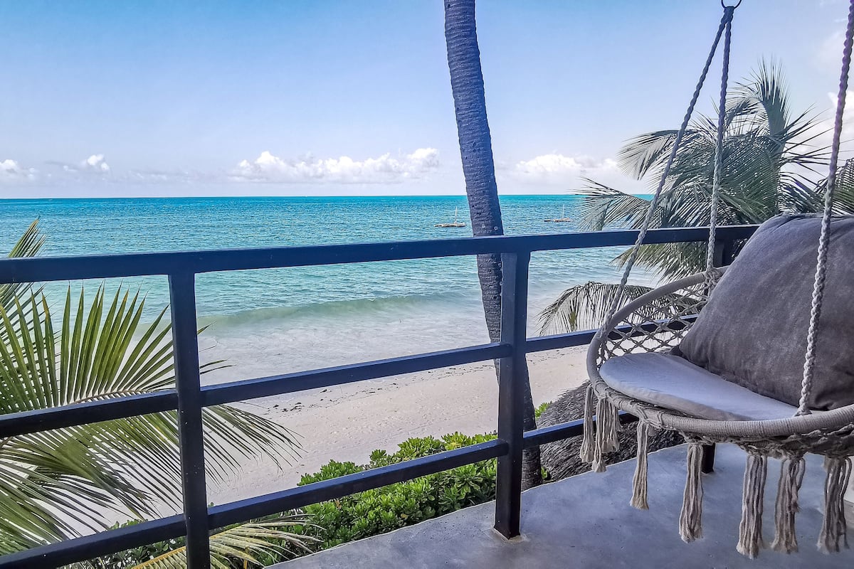 A balcony with a swing chair overlooking a beach.