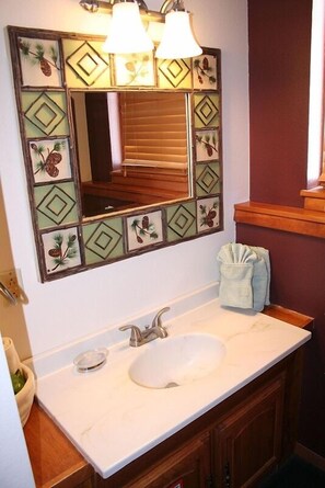 A bathroom with a white sink, wooden cabinets, and a mirror with a geometric tile design. - Timber Creek Chalets: 5 1 Bedroom Chalet (Estes Park)