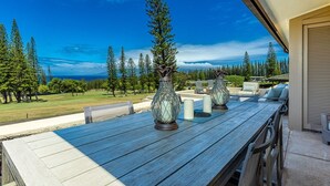 Een houten tafel met decoratieve glazen vazen en kaarsen, voor een achtergrond van een weelderig landschap met bomen en een helderblauwe lucht.