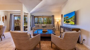 Een ruime woonkamer met een groot raam, een bank, twee fauteuils, een salontafel en een flatscreen-televisie aan de muur.