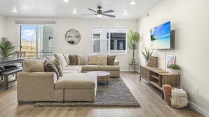 Un salon moderne avec un canapé d’angle, une table basse ronde et un téléviseur fixé au mur.