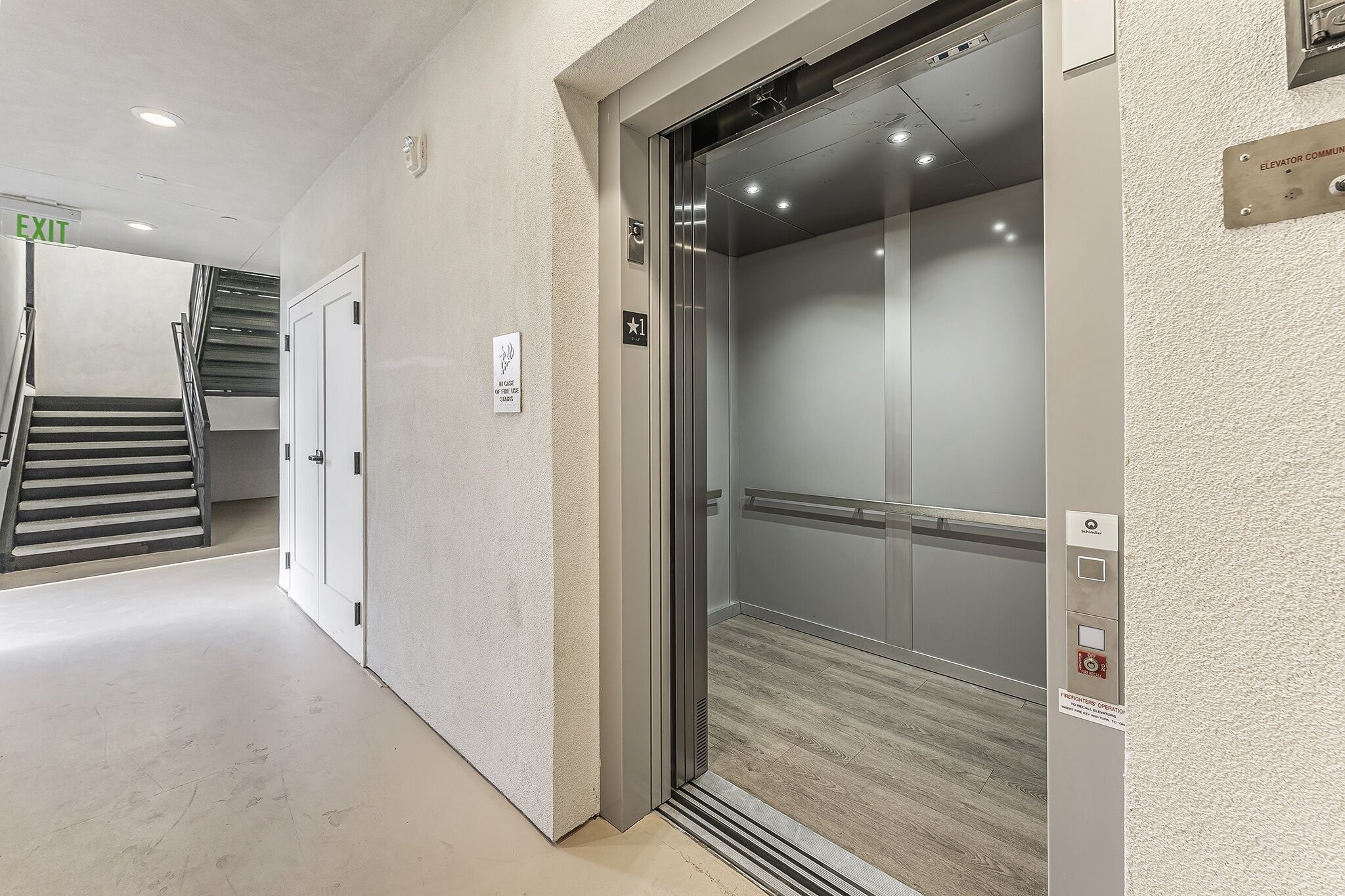 Een lift met glazen deur, een brandmelder en een bordje met de tekst 'liftgemeenschap'.