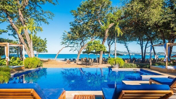 Ein Poolbereich mit Holzliegen und Blick auf das Meer.