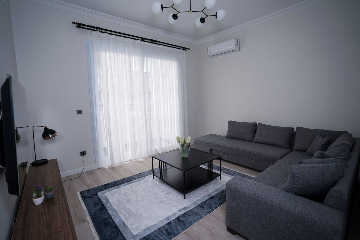 A modern living room with a grey sofa, a black coffee table, and a wooden side table with plants.