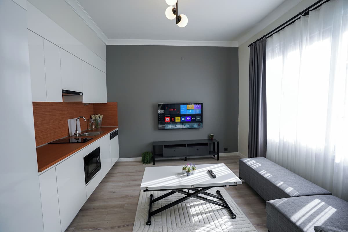 A modern living room with a sofa, a coffee table, a TV, and a kitchen area with cabinets and a countertop.