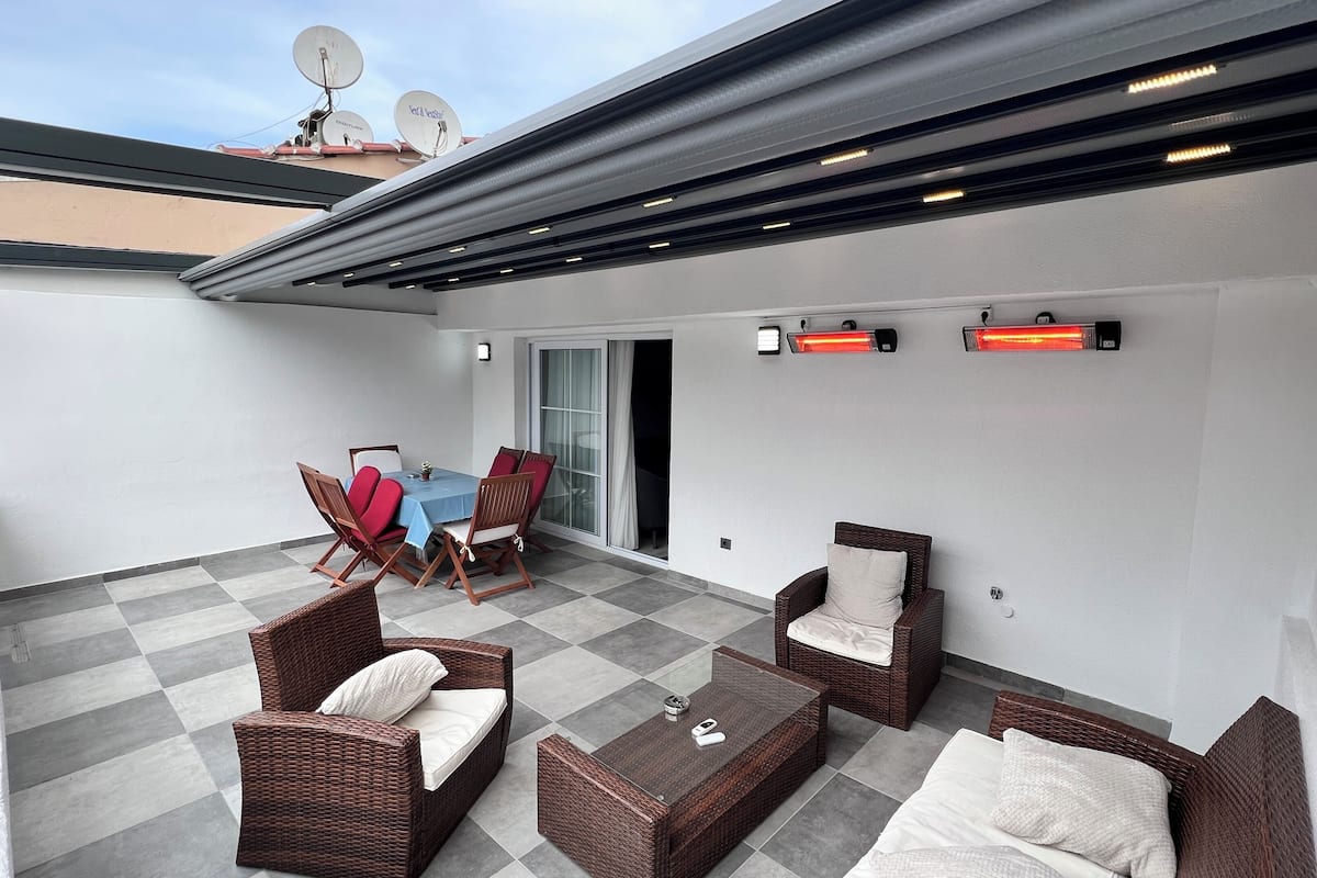 A covered patio area with a table and chairs, a sofa, and a heat lamp.