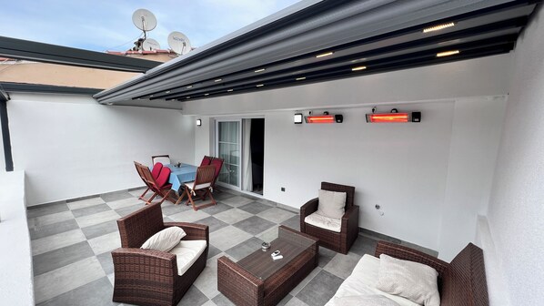 A covered patio area with a table and chairs, a sofa, and a heat lamp. - Merkuri Apart (Istanbul)