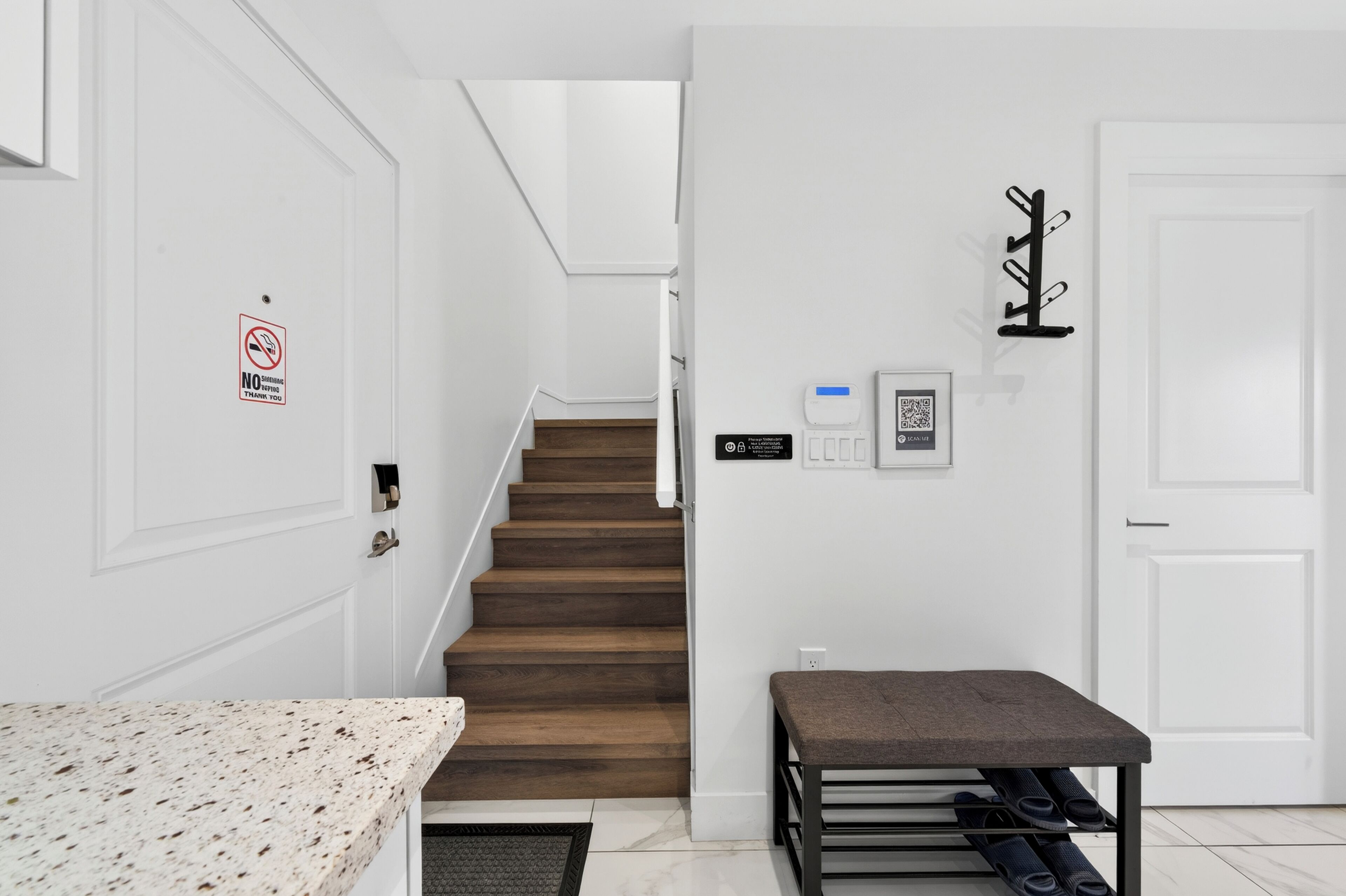 A hallway with a wooden staircase, a bench, a coat rack, and a door with a no smoking sign.