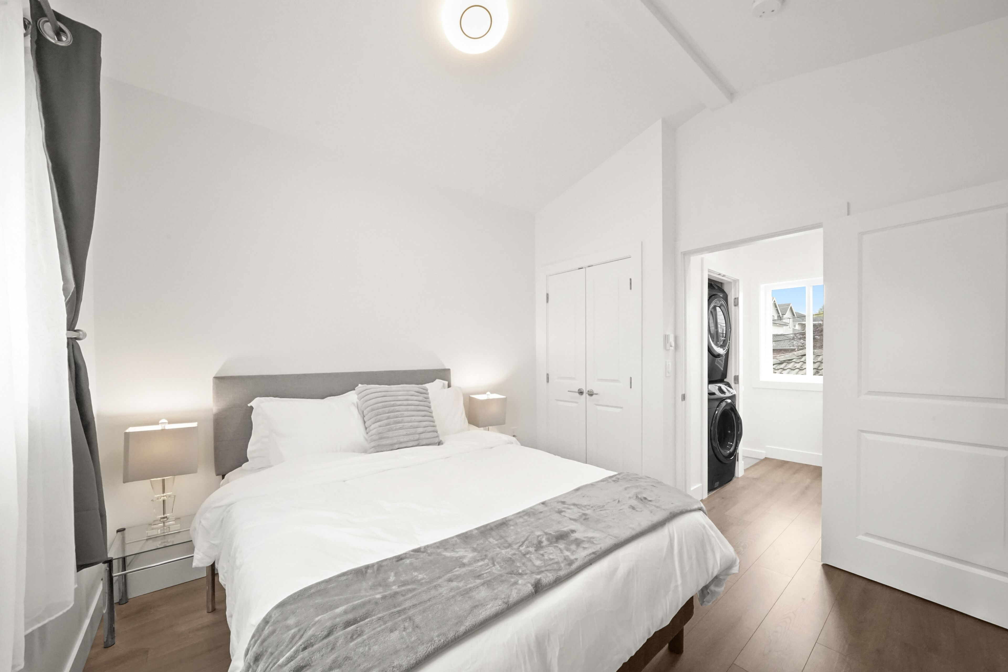 Habitación de hotel con una cama grande, una mesita de noche con lámpara, un armario y vistas al exterior.