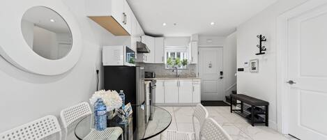 A modern kitchen with white cabinets, a round mirror, and a glass dining table with white chairs.