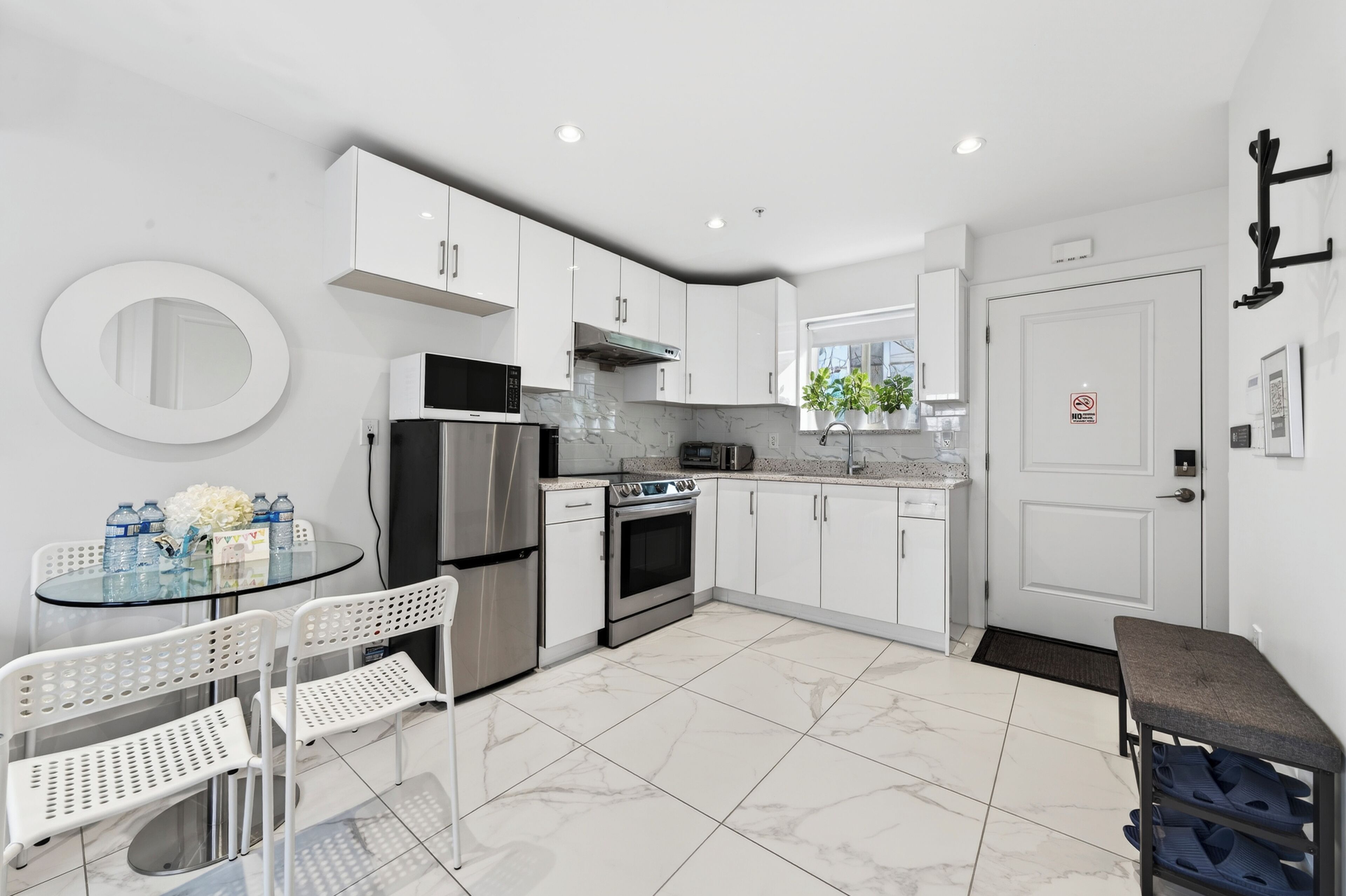 Eine moderne Küche mit weißen Schränken, einem Edelstahl-Kühlschrank, einer Mikrowelle, einem Backofen und einem Essbereich mit einem Glastisch und weißen Stühlen.