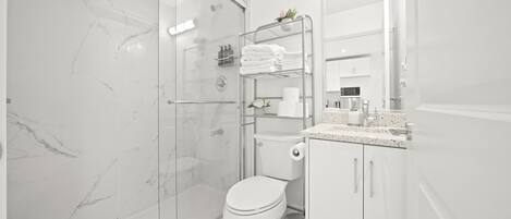A modern bathroom with a glass-enclosed shower, a toilet, and a sink area with a countertop.