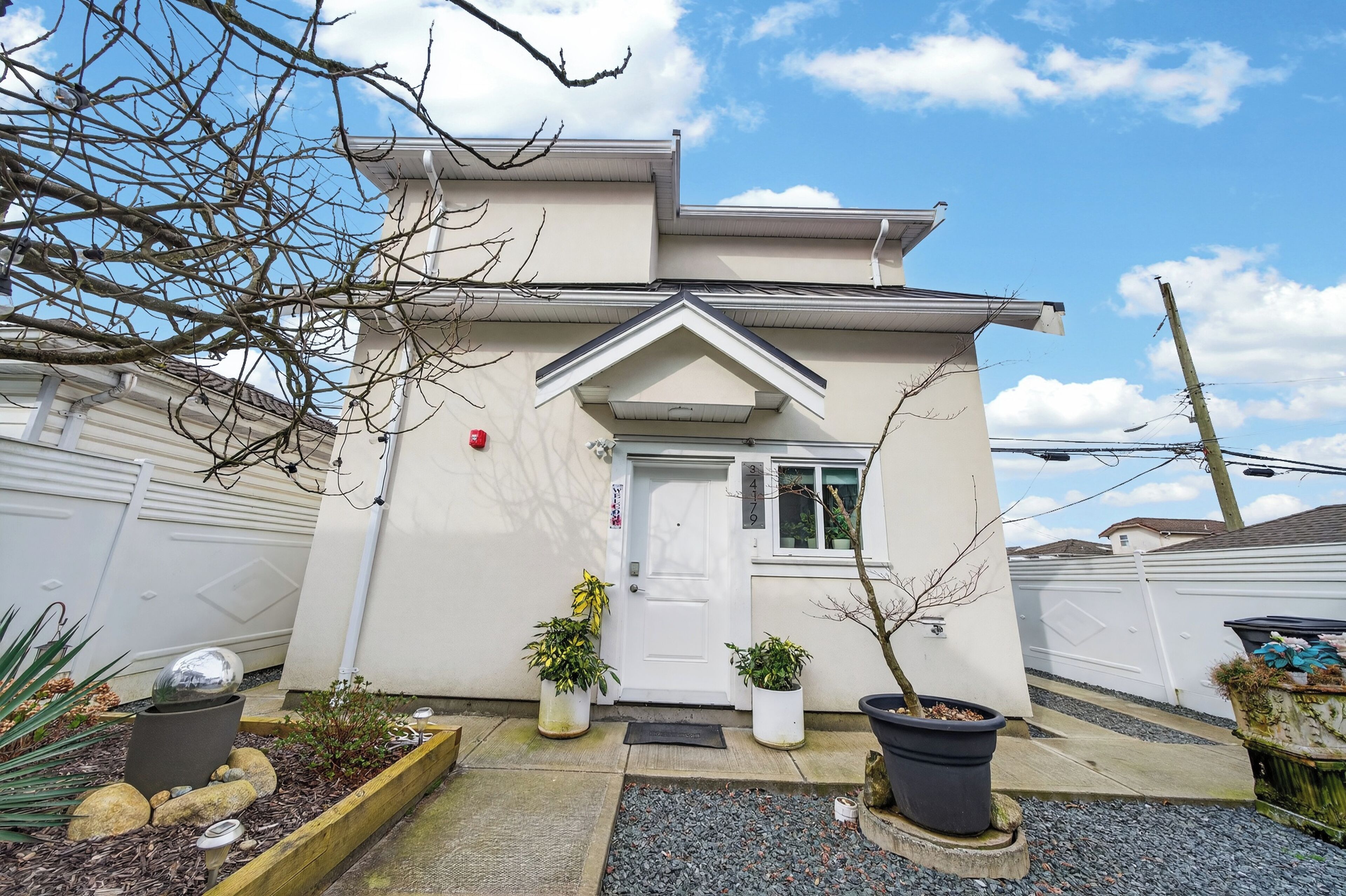 A two-story house with a white exterior, a front door, and potted plants.