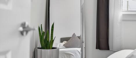 Une chambre d’hôtel moderne avec un grand miroir, une plante en pot, un lit avec une literie blanche et une fenêtre avec des rideaux.