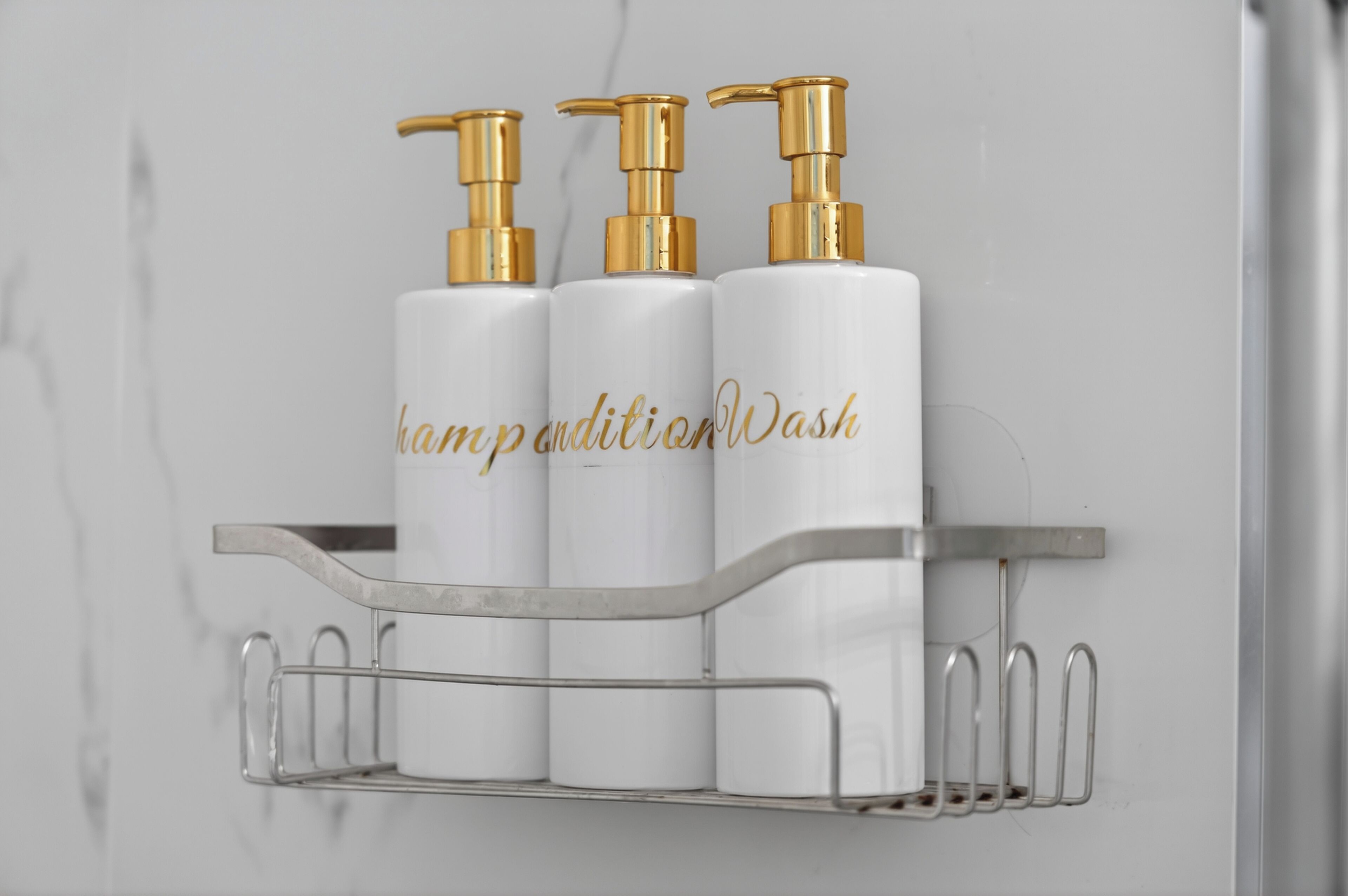 A bathroom shelf with three white bottles and gold pumps, labeled 'kampotionWash.'