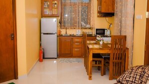 Een kleine keuken met houten kastjes, een koelkast, een magnetron en een eettafel met stoelen.