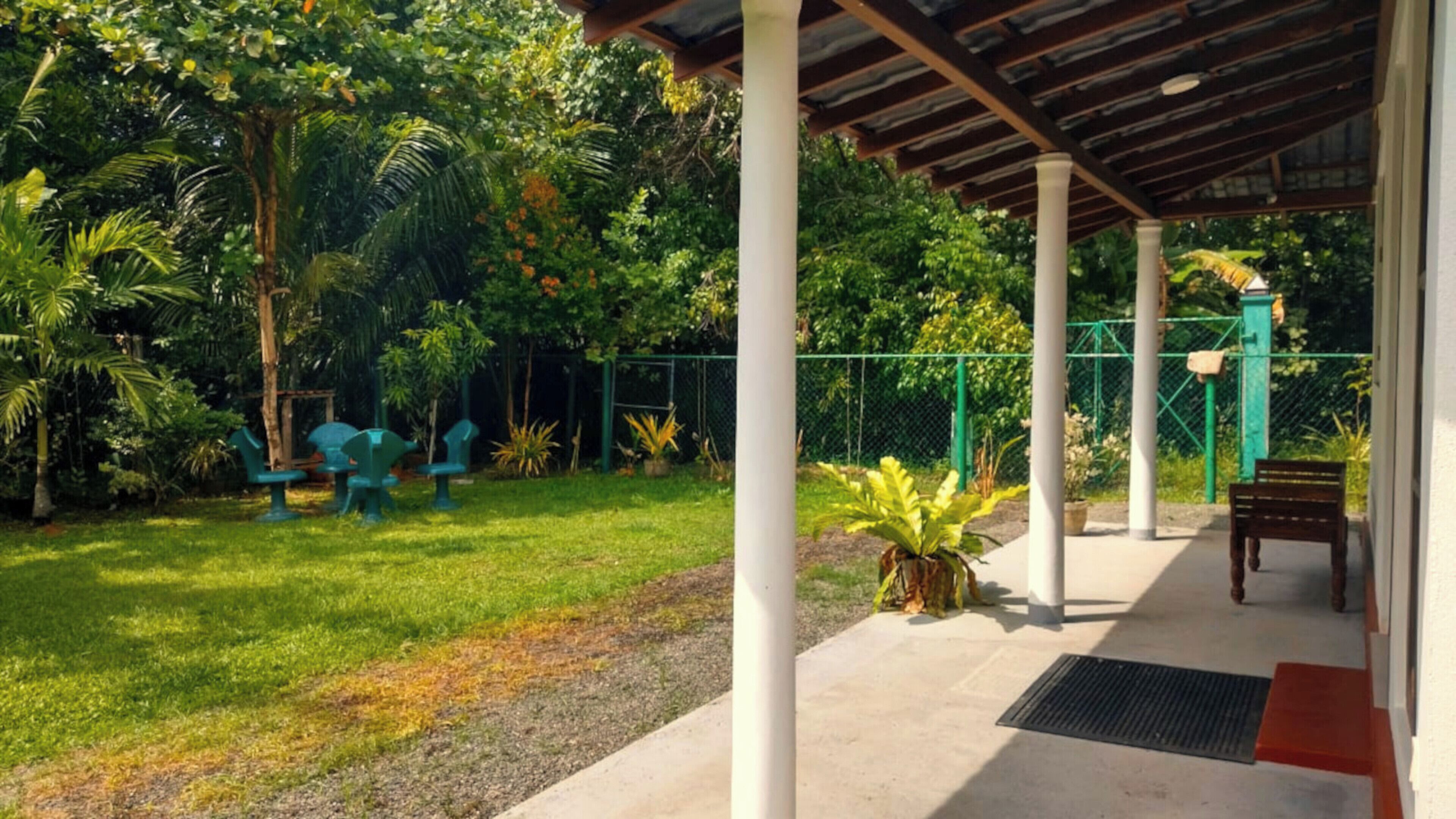 Un espacio al aire libre techado con piso de concreto, rodeado de follaje y una cerca.