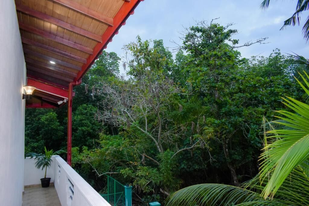 Un balcone coperto con tetto rosso, circondato da rigogliosa vegetazione e alberi.