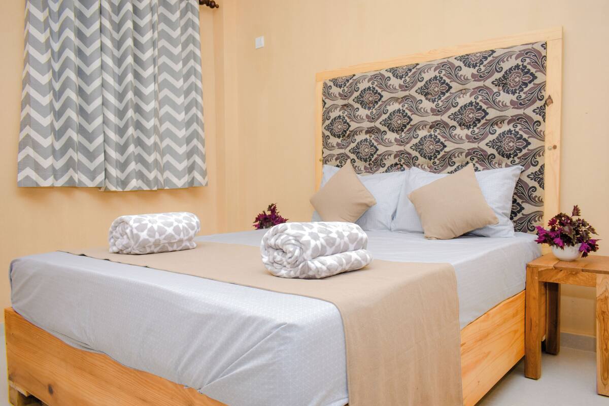 Una cama doble con dos almohadas y una colcha, y un cabecero estampado.