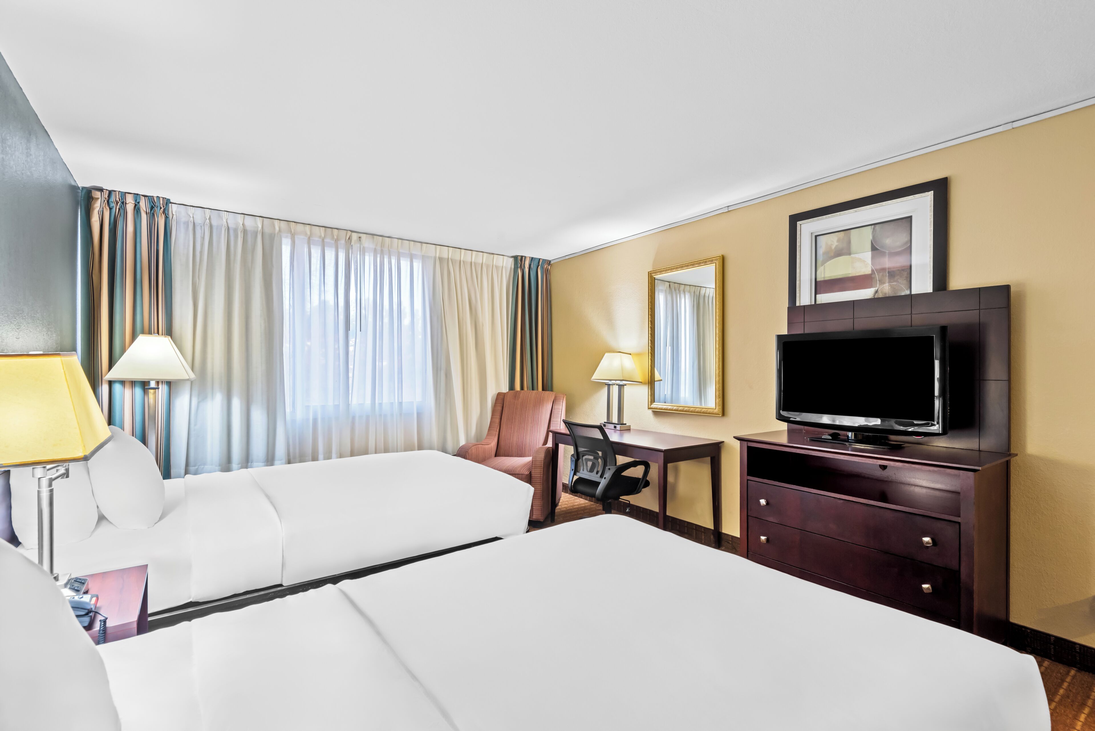 A hotel room with two beds, a desk, a chair, a television, and a window with curtains.