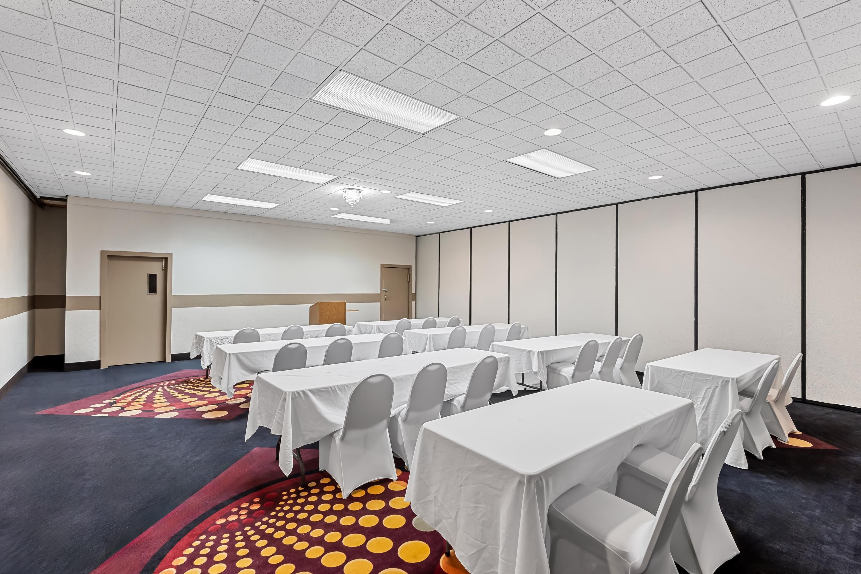 A conference room with multiple tables and chairs, a patterned carpet, and a ceiling with recessed lighting.