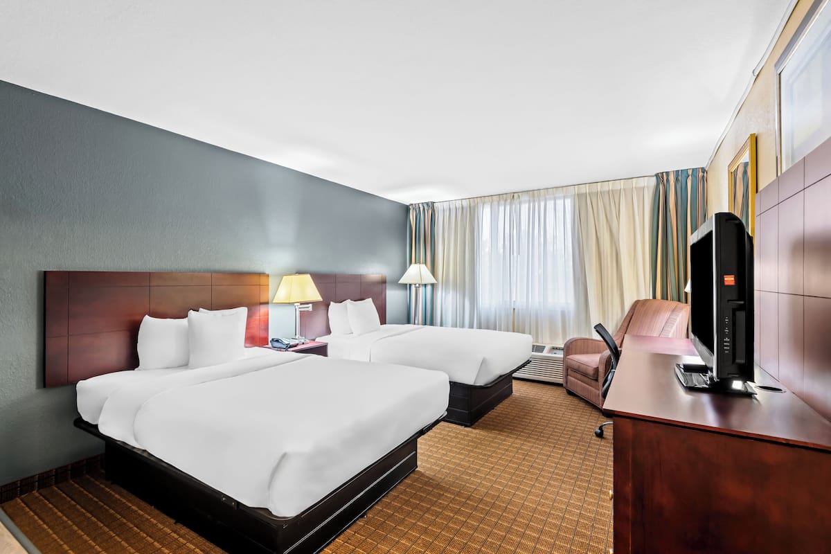 Ein Hotelzimmer mit zwei Betten, einem Schreibtisch mit Computer, einem Fernseher und einem Sessel.