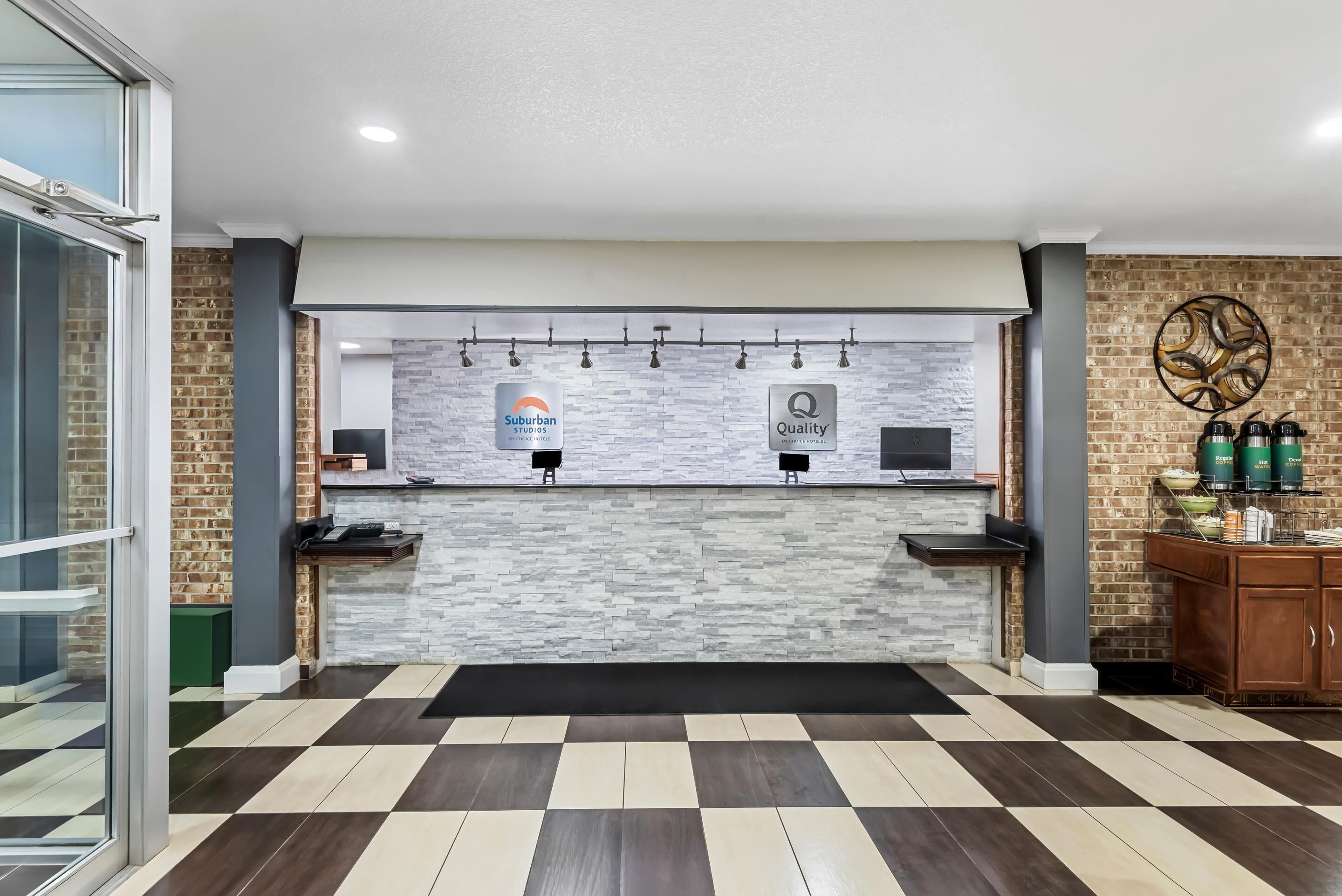 A reception area with a check-in counter, two monitors, a stone wall, and a patterned floor.