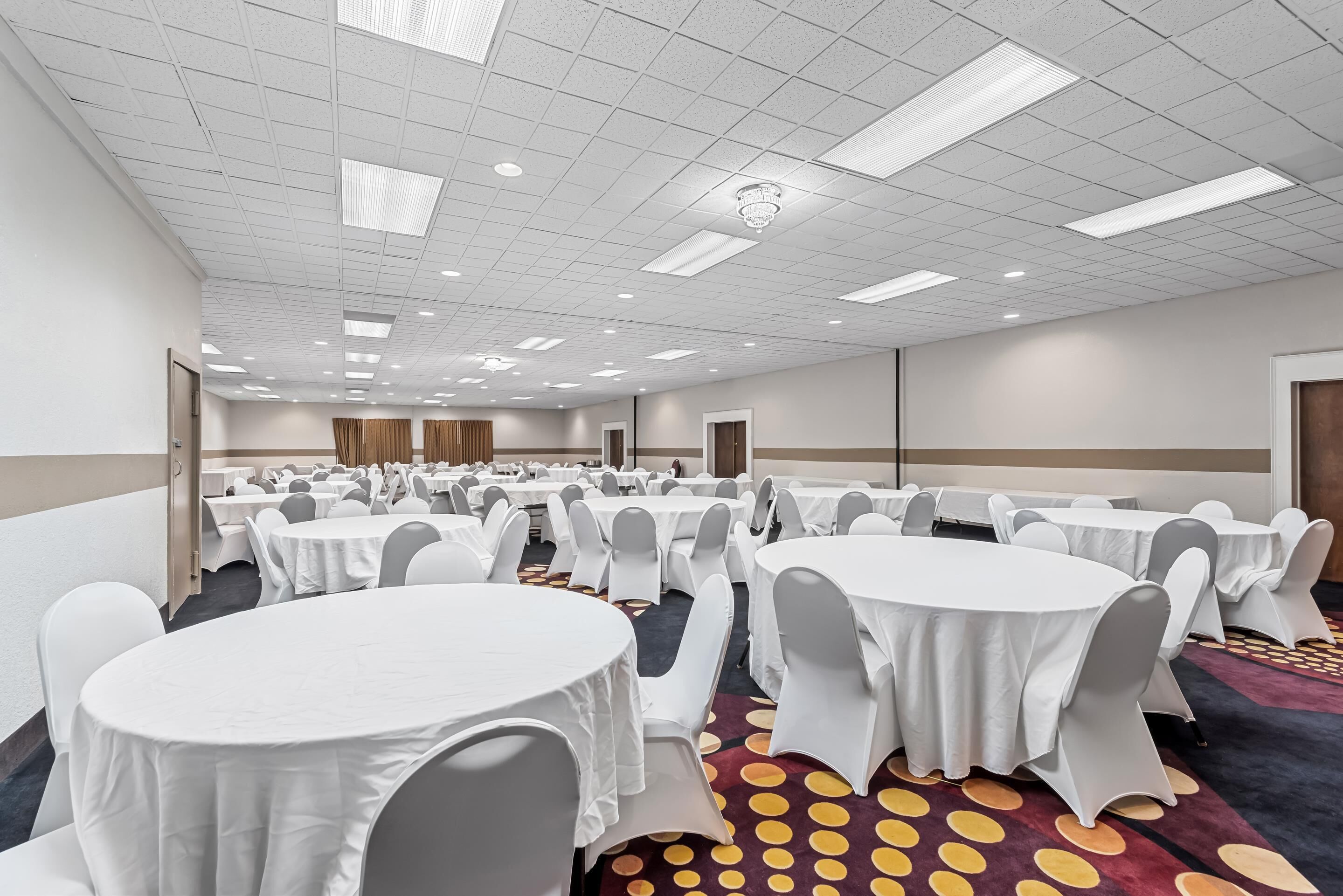 A large conference room with multiple round tables covered in white tablecloths and grey chairs, arranged in rows.