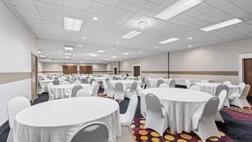 A large conference room with multiple round tables covered in white tablecloths and grey chairs, arranged in rows.